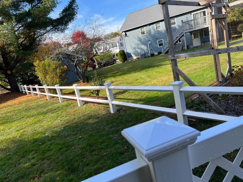 Crew-installed white vinyl post-and-rail fence in a residential backyard