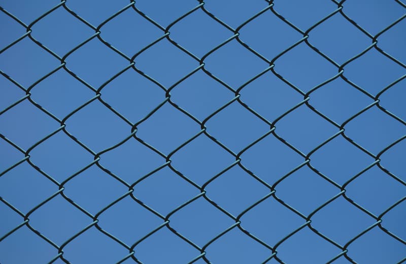 Galvanized chain-link security fence photographed against a clear blue sky