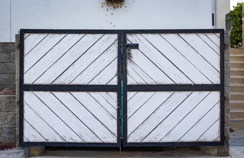 White diagonal-board double gate with a dark steel frame in front of a home