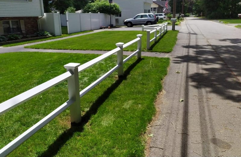 White vinyl post-and-rail fence running along a neighborhood sidewalk