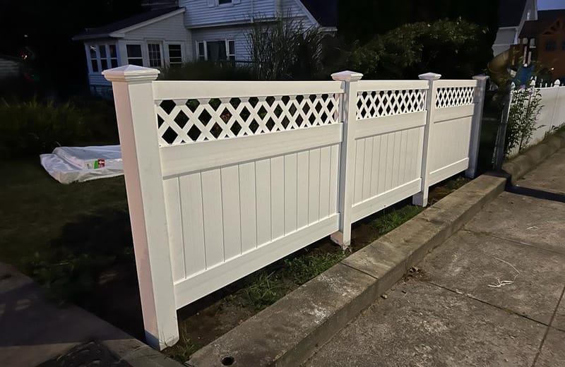 White vinyl privacy fence with decorative lattice top panels installed along a walkway
