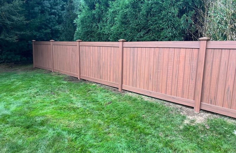 Woodgrain vinyl privacy fence panels along a landscaped lawn