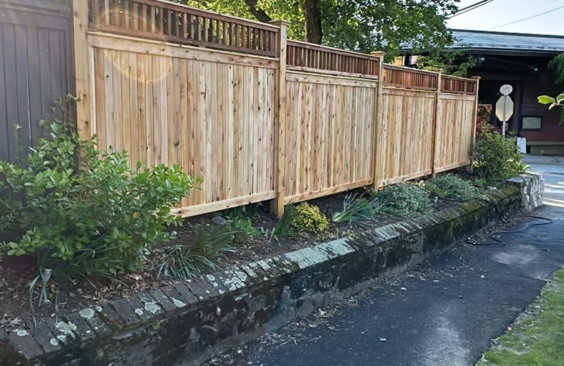 Cedar privacy fence with lattice top running along a stone retaining wall